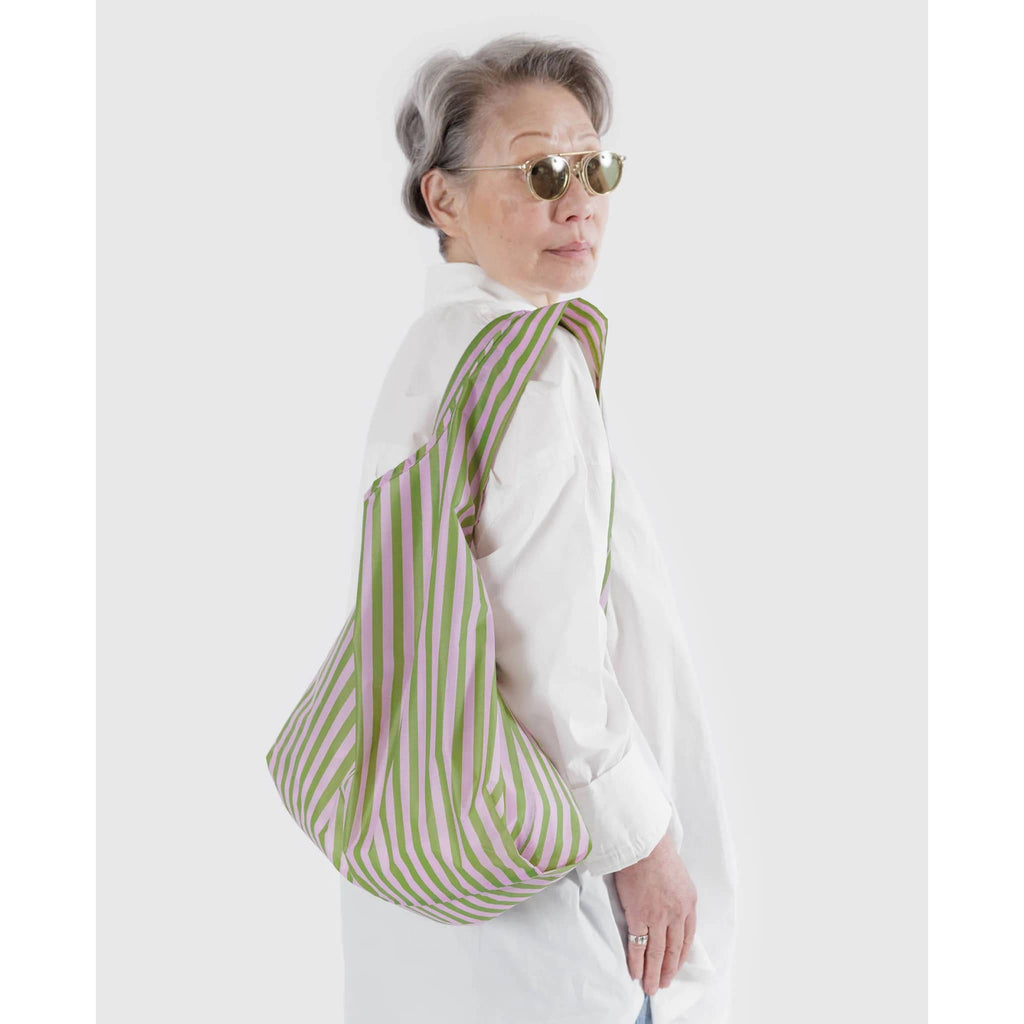 Baggu standard size eco-friendly recycled ripstop nylon reusable tote bag with lilac and green avocado candy stripe print, on model's shoulder.