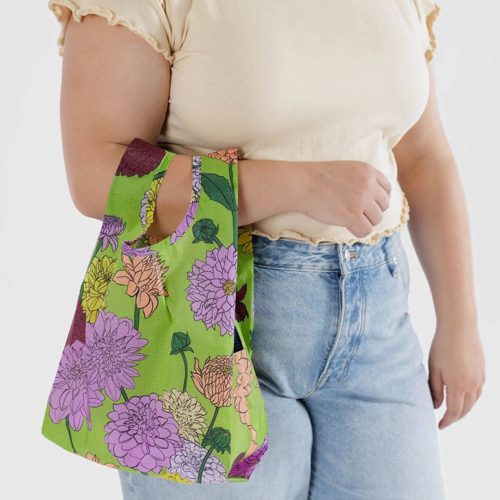 Baggu baby size eco-friendly recycled ripstop nylon reusable tote bag with the Dahlia print on a green background, on model's arm.