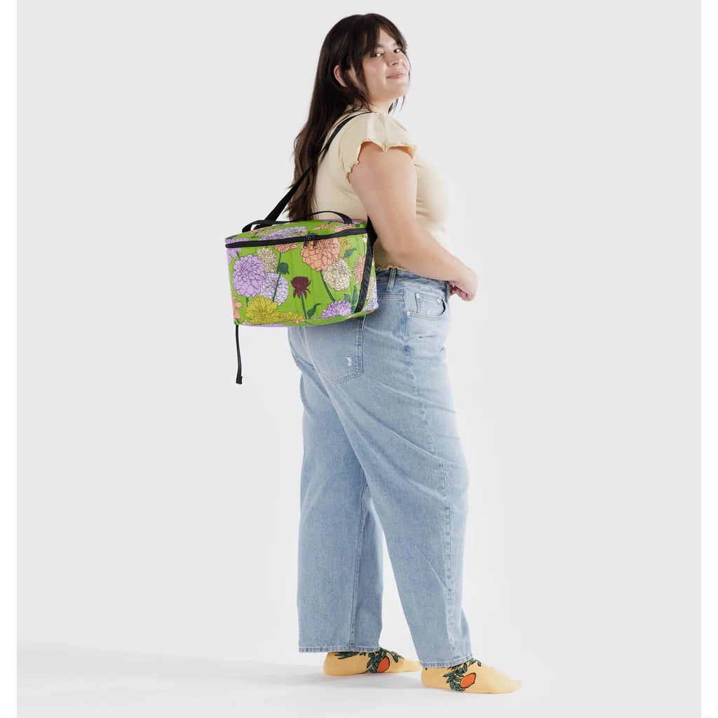 Baggu Insulated Puffy Cooler Bag with Dahlia print on a green backdrop with black zipper, shoulder strap and handle, on model's shoulder.