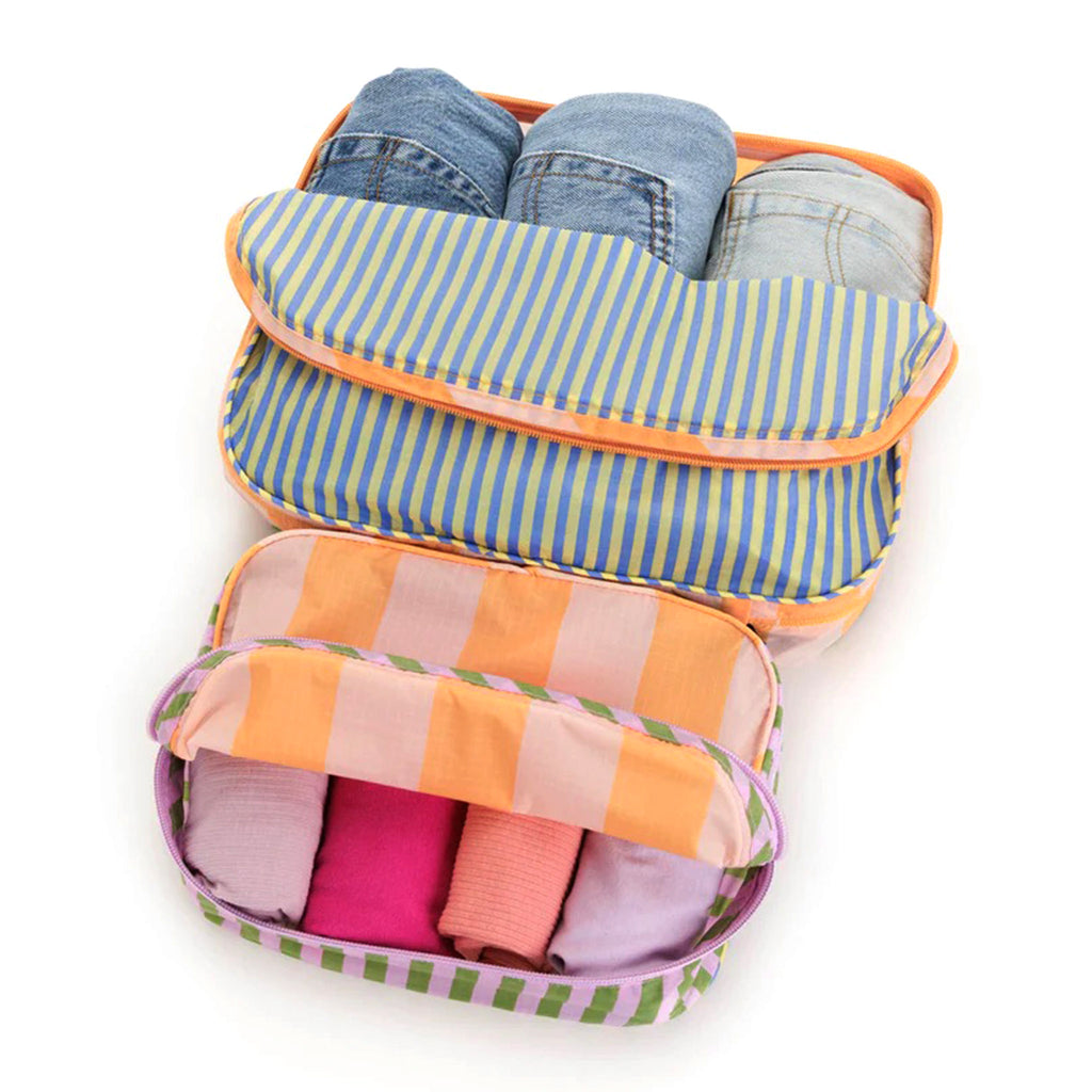 Baggu reusable recycled ripstop nylon packing cube set of 2, both sizes have the colorful hotel stripes prints, partially unzipped and filled with clothing.