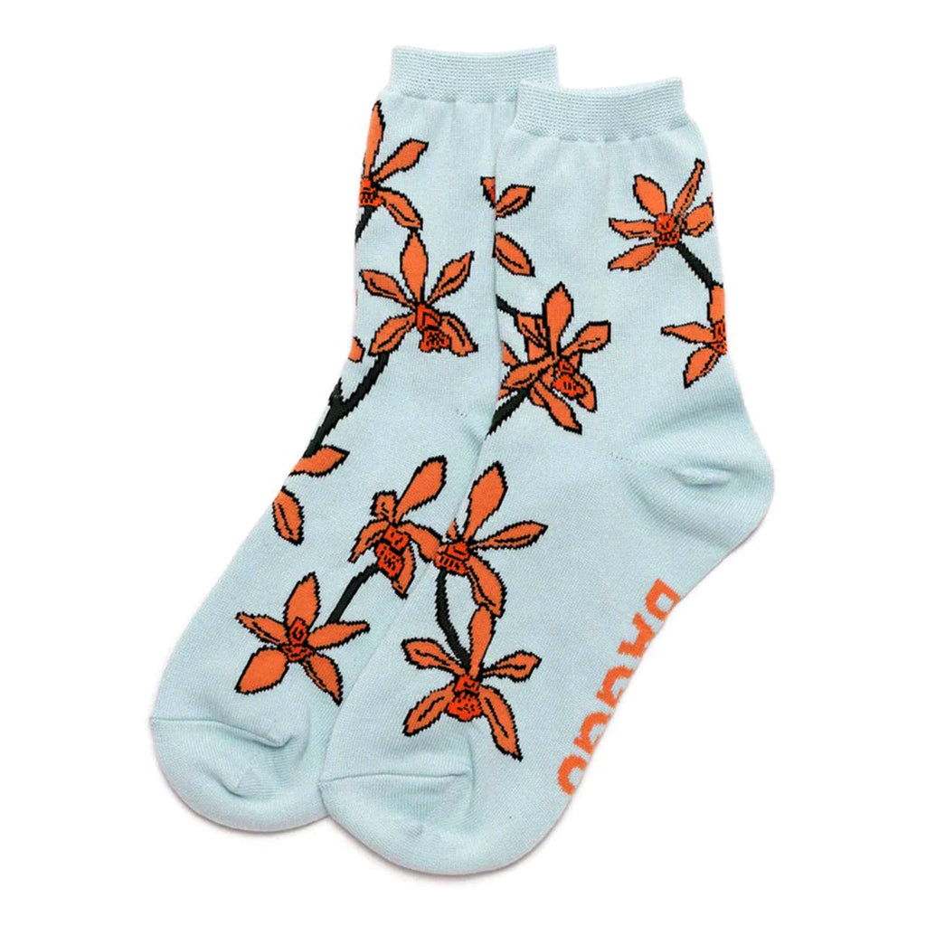 Baggu bamboo rayon unisex crew socks with orange orchids on a pale blue background, flat.