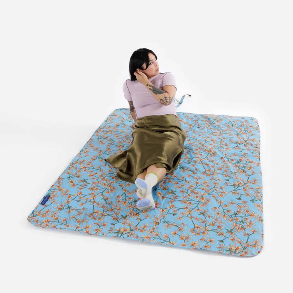 Baggu orchid puffy recycled ripstop nylon and polyester picnic blanket, flat with a model sitting on it.