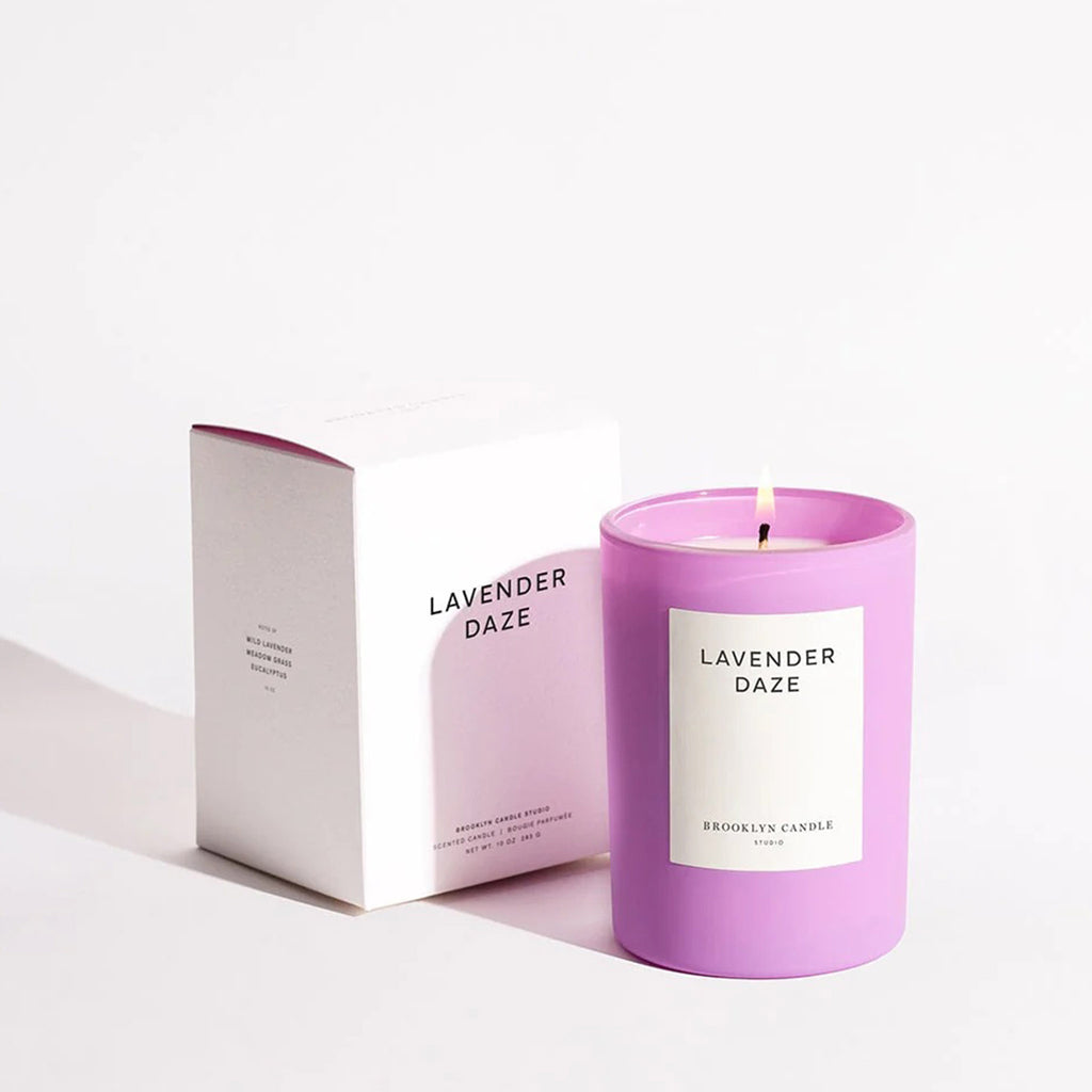 Brooklyn Candle Studio Lavender Daze scented candle in matte lilac glass vessel with white label and lit wick, beside white gift box.