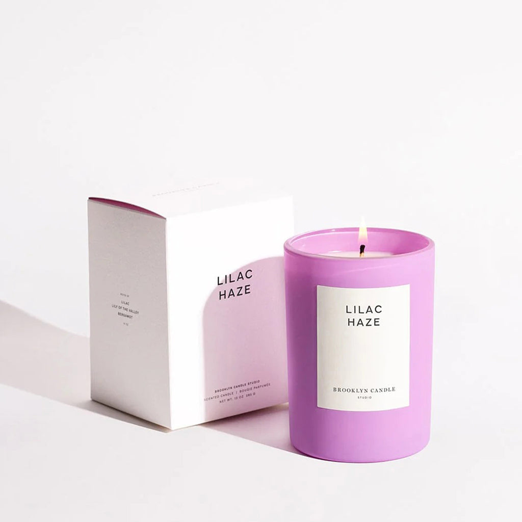 Brooklyn Candle Studio Lilac Haze scented candle in matte lilac glass vessel with white label and lit wick, beside white gift box.