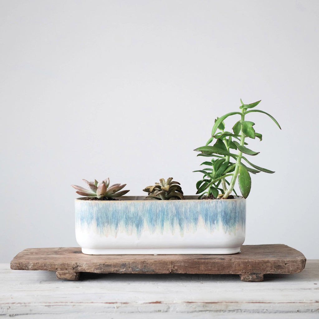 Creative Co-op Stoneware 3 Section Window Planter with a blue and white reactive glaze finish, shown with plants and sitting on a wood board on a weathered white wood surface.