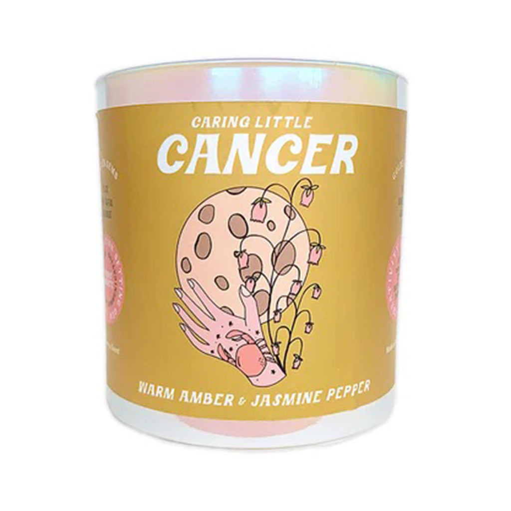 Golden Gems Caring Little Cancer Warm Amber and Jasmine Pepper scented soy wax candle with illustrated mustard yellow label on an iridescent white glass tumbler, front view.