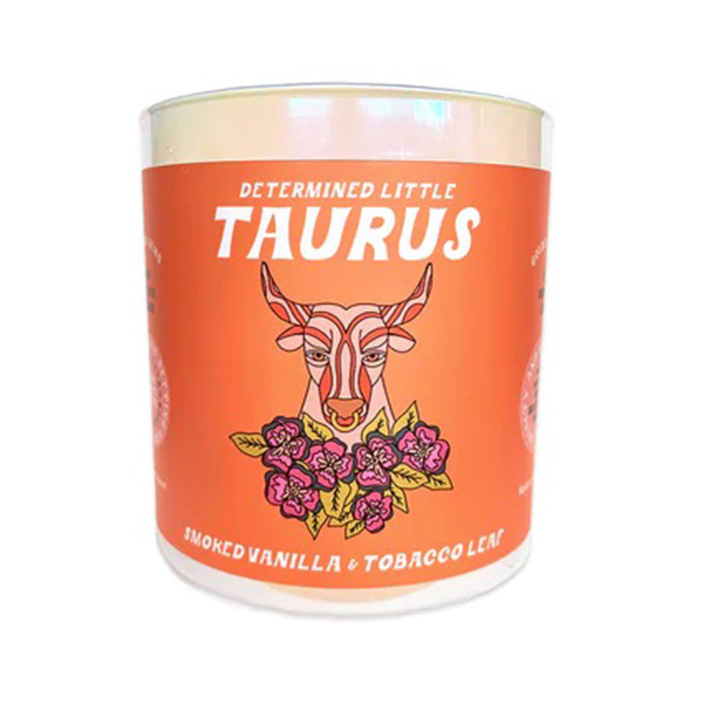Golden Gems Determined Little Taurus Smoked Vanilla and Tobacco Leaf  scented soy wax candle with illustrated orange label on an iridescent white glass tumbler, front view.