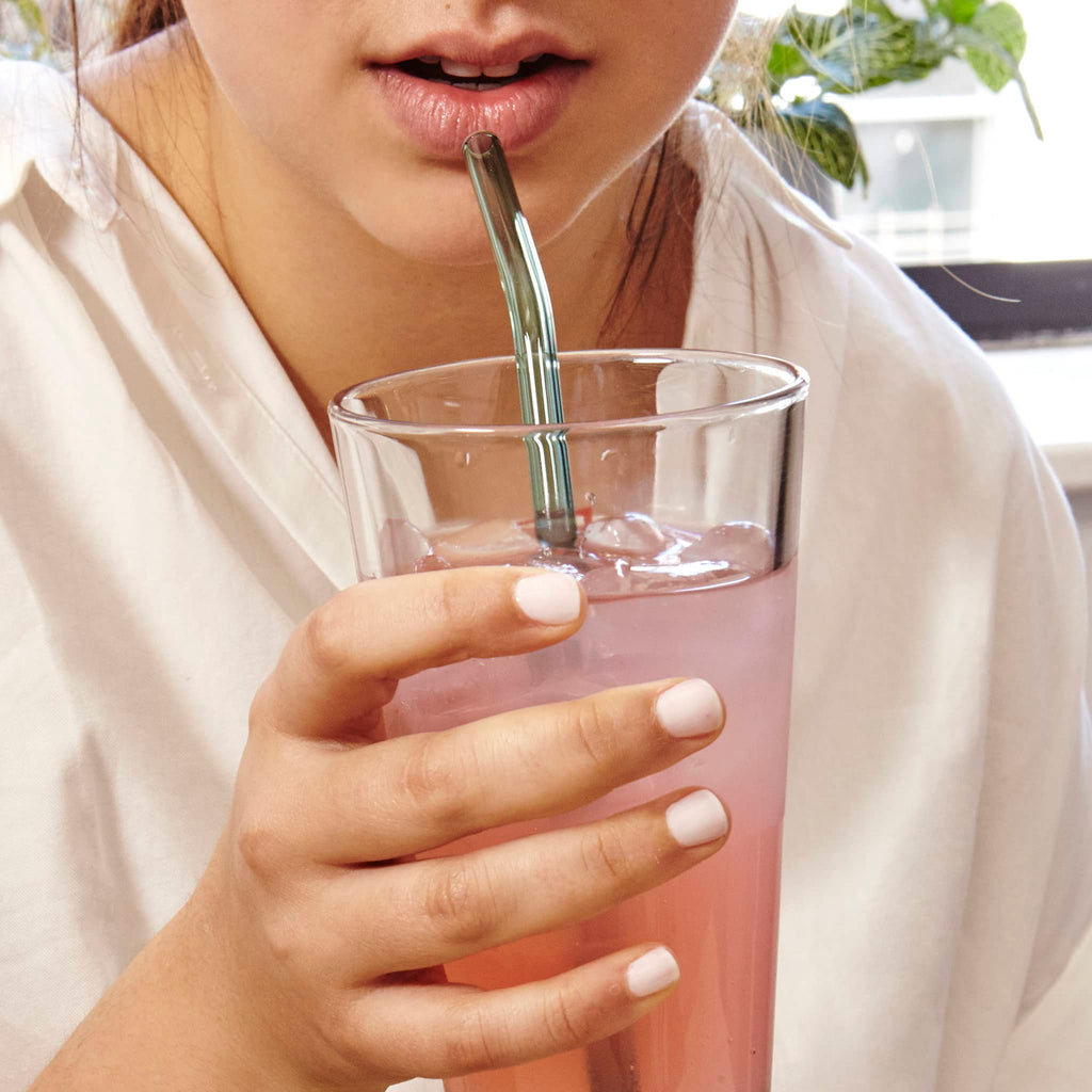 Kikkerland Colorful Reusable Glass Straws, curved straw in a pink drink with model holding the glass.