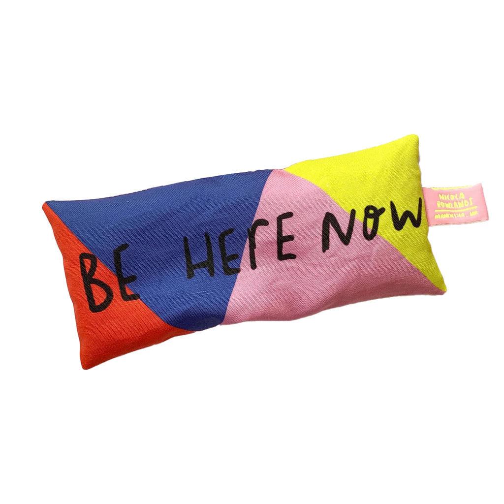 Nicola Rowlands lavender scented weighted eye pillow in red, blue, pink and yellow color blocking  with "be here now" in black lettering.
