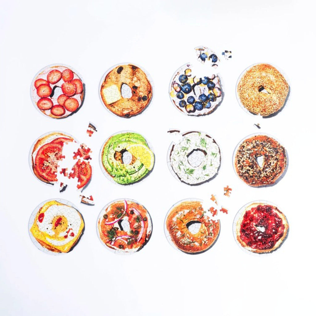 Piecework Puzzles Box of Bagels, set of 12 round mini puzzles in various states of completion.