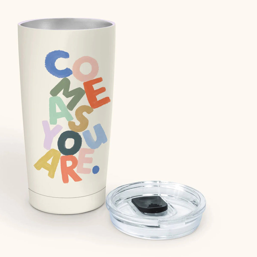 Studio Oh! 17 ounce stainless steel insulated tumbler with clear lid beside it. Off-white tumbler has "come as you are" in colorful, jumbled letters on the front.