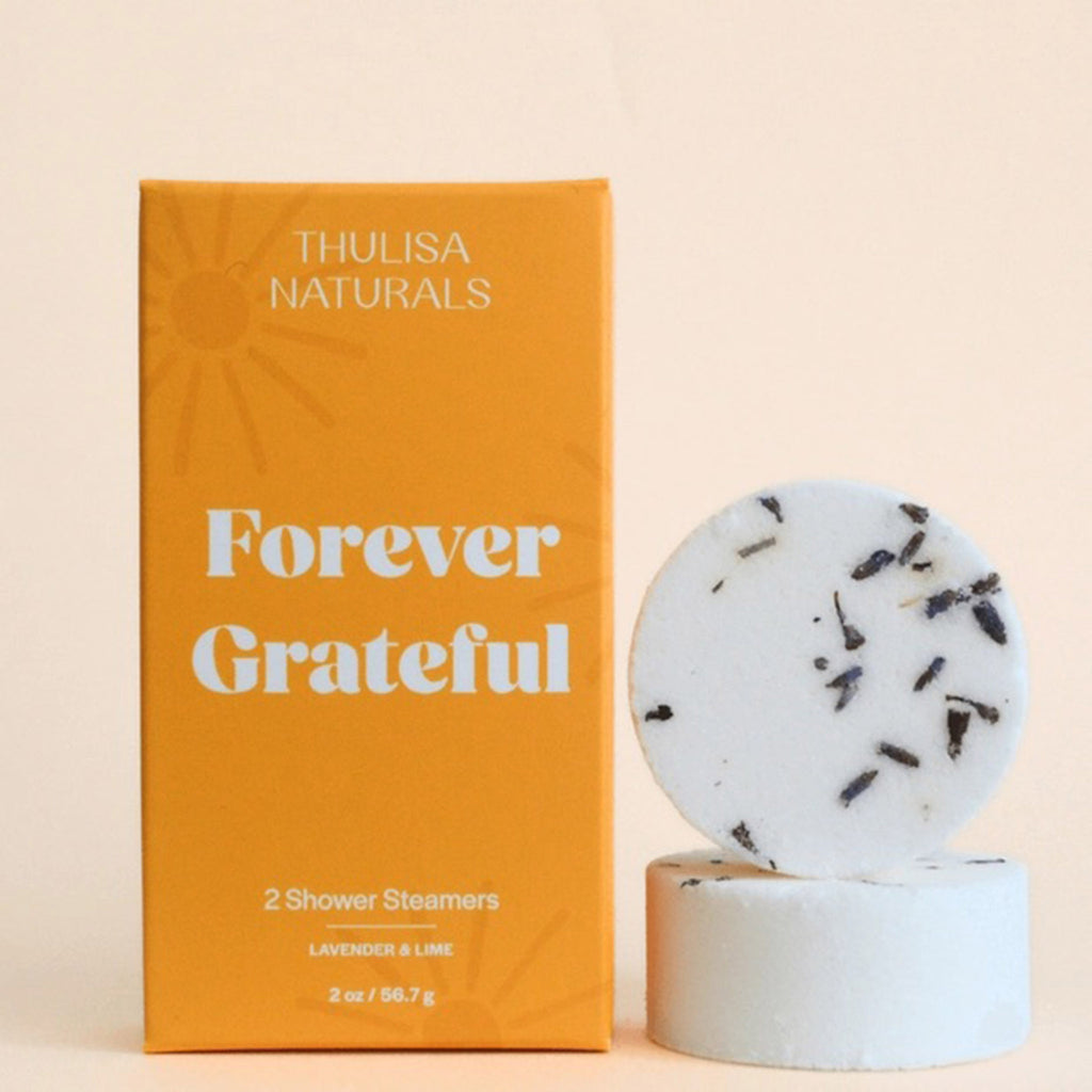 Thulisa Naturals Lavender and Lime Shower Steamers 2 Pack in yellow box with sun illustrations and "Forever Grateful" in white lettering, front view with 2 shower steamers stacked beside it.
