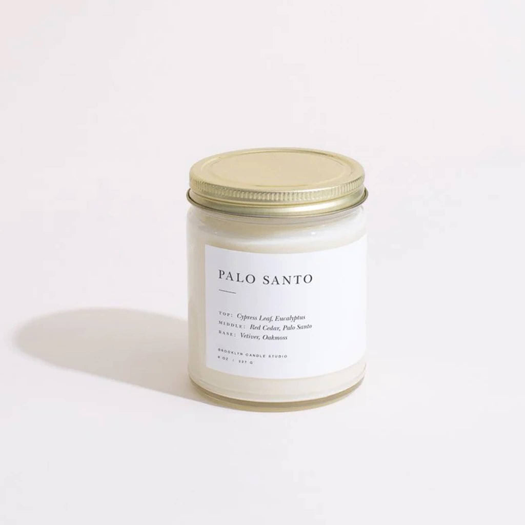Palo Santo scented candle in a straight sided clear glass jar with minimalist label and brushed gold screw-on lid.