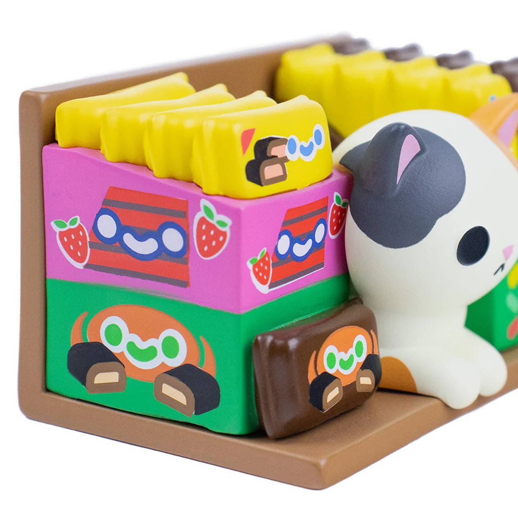 Detail of white and gray cat figurine nestled among candy packaging.