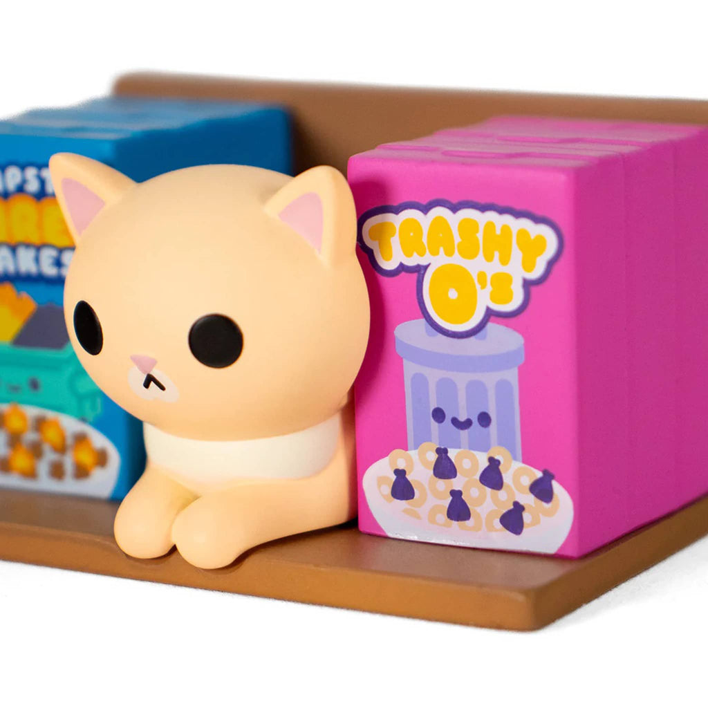 Detail of tabby cat figurine next to a pink box labeled 'Trashy O's' on a brown surface.