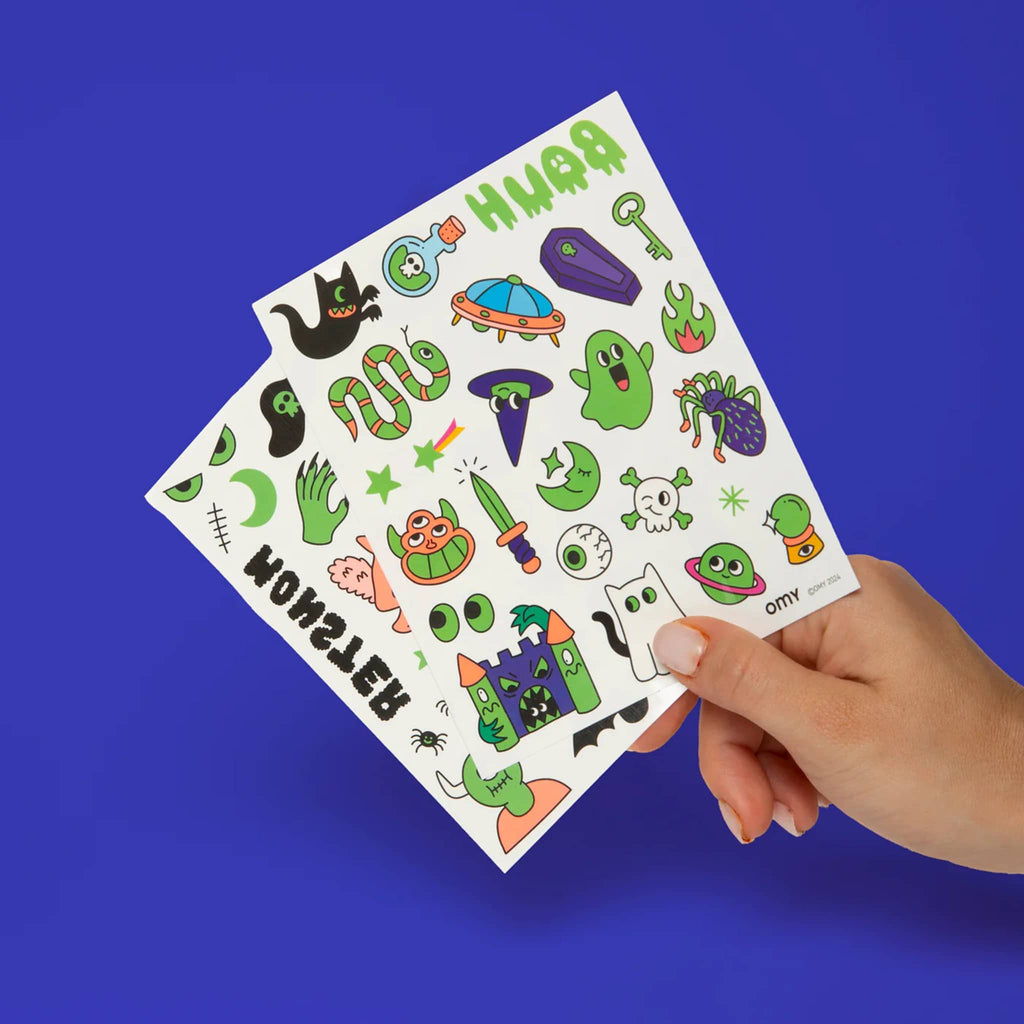 Hand holding a sheet of colorful Halloween-themed glow in the dark temporary tattoos against a blue background.