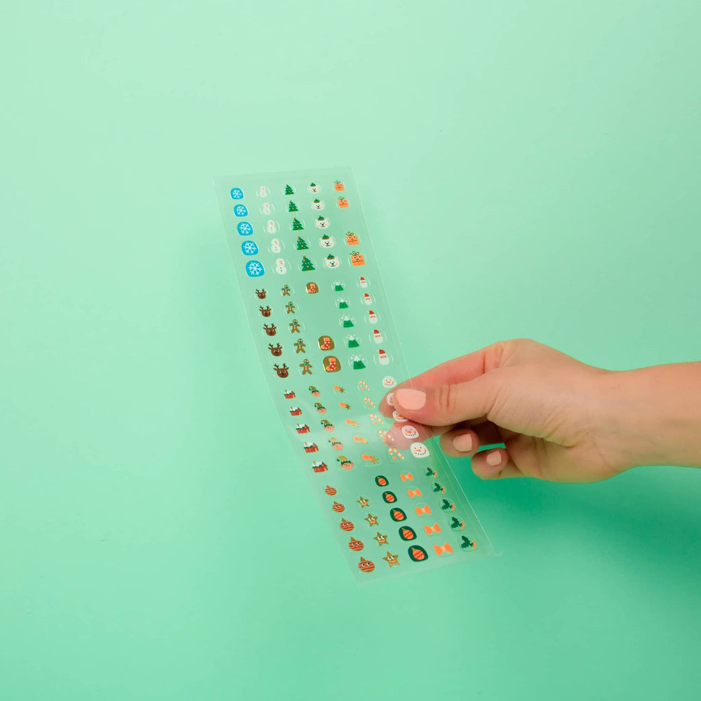 Hand holding a clear sheet with small decorative nail stickers against a light green background.