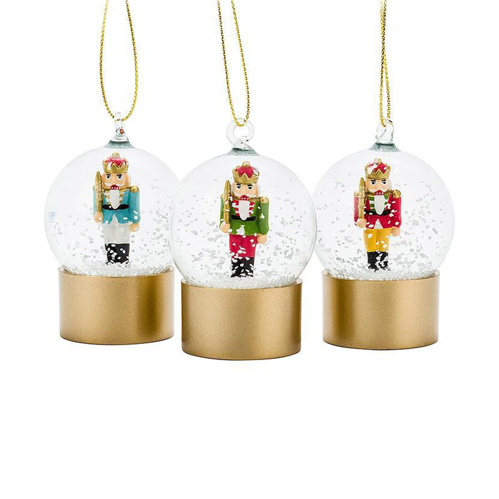 Abbott small clear snow globes on gold bases with a blue, green or red nutcracker inside with a gold string for hanging on a tree.