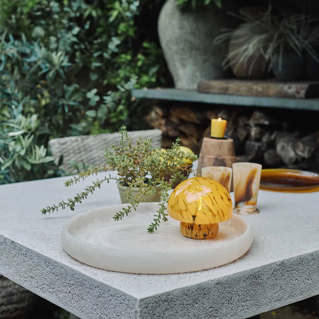 Yellow glass mushroom-shaped cordless led table lamp on an outdoor table.