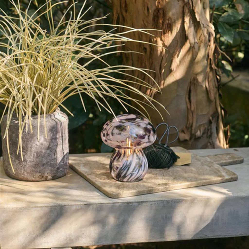 Decorative mushroom lamp on a stone surface with plants and natural elements in the background.