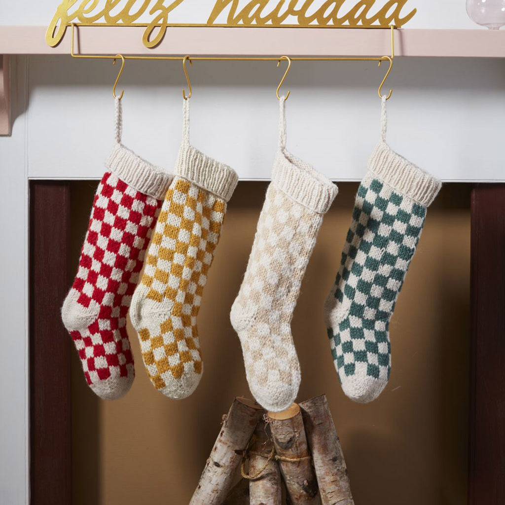 Accent Decor Damier checkerboard pattern knit holiday Christmas stockings in 4 colors, hanging by hooks on a fireplace mantel.
