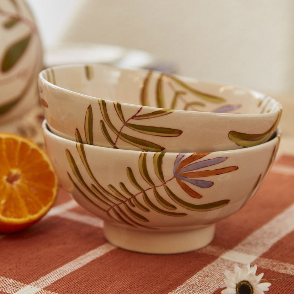 Accent Decor Parable Bird Ceramic Bowl with a hand-painted red, orange and green bird and leaf design on a cream backdrop, side view of 2 bowls stacked to show leaf design.