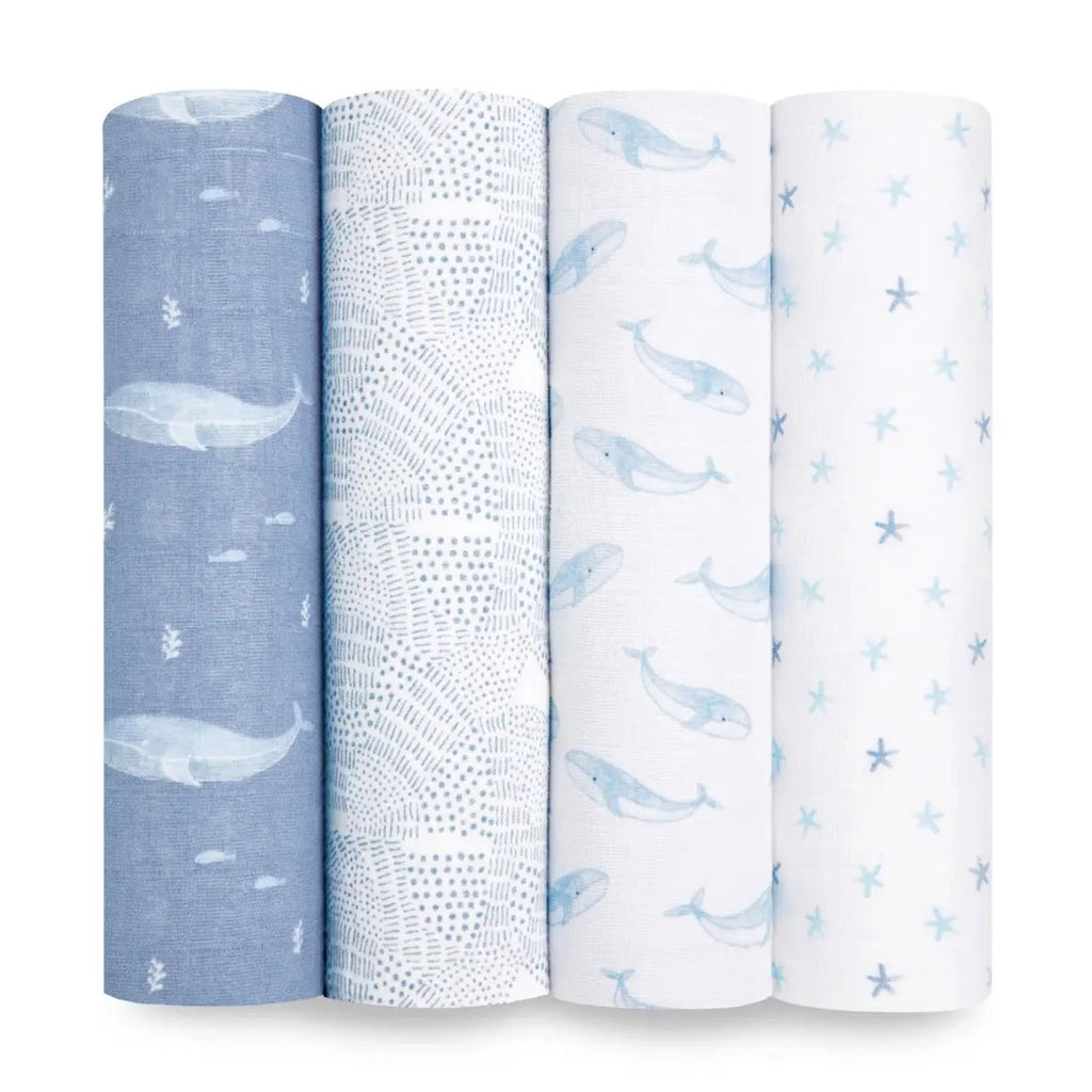 Aden + Anais Oceanic set of 4 organic cotton muslin baby swaddle blankets rolled up, prints have whales, waves and starfish in blue and white.