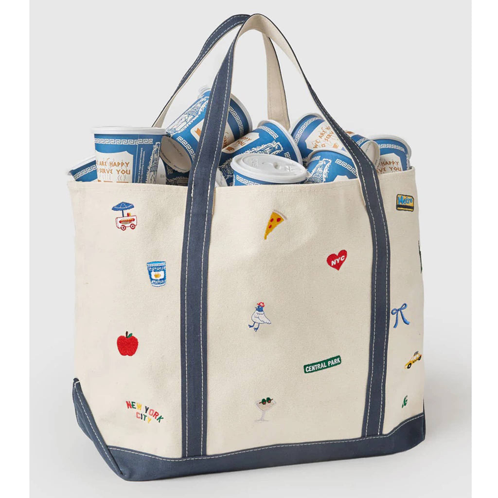 Natural cotton canvas tote bag with various NYC icons embroidered, filled with paper greek cups, front angle view, on a gray background.
