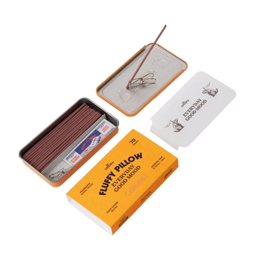 Ameico Collins Fluffy Pillow sandalwood scented incense sticks in yellow tin packaging, open with contents shown including outer sleeve and an incense clip holding a brown incense stick on the overturned lid.