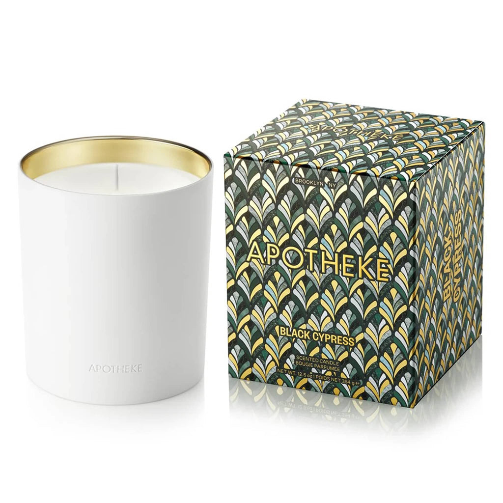 Apotheke Black Cypress 12.5 ounce scented candle in white ceramic vessel with gold interior, shown beside a green and gold art deco printed box.