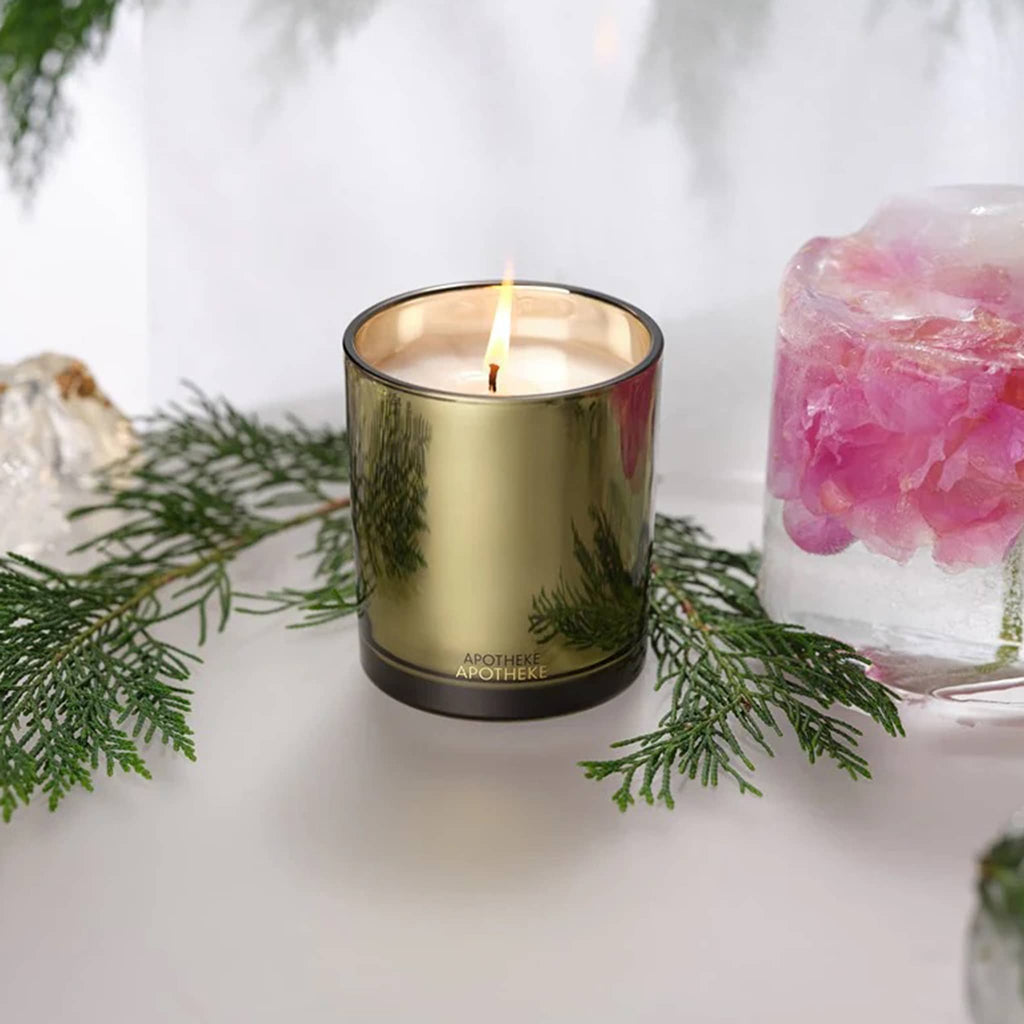Olive gold metallic candle with greenery and ice with pink flowers on a white surface.