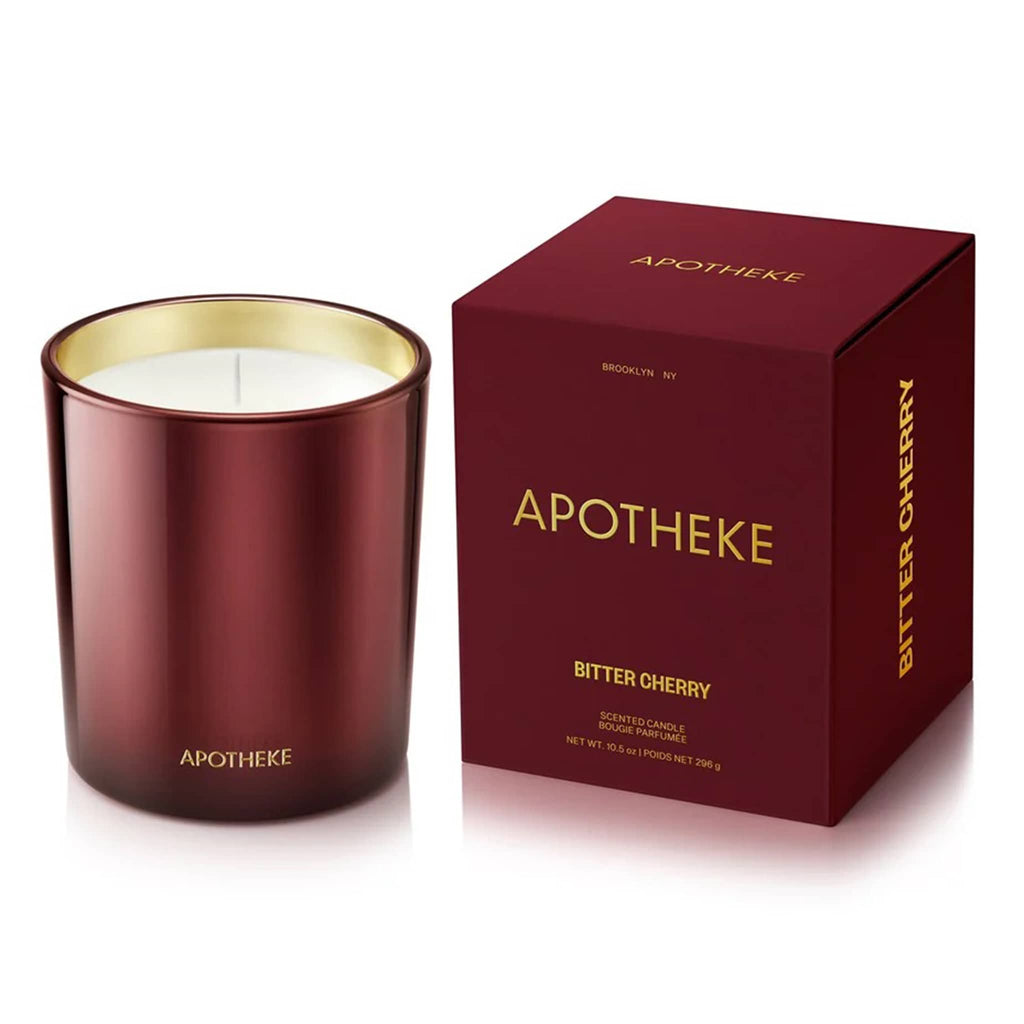 Apotheke 10.5 ounce Bitter Cherry scented soy wax blend candle in deep cherry red glass vessel with gold interior, next to matching gift box with gold lettering.