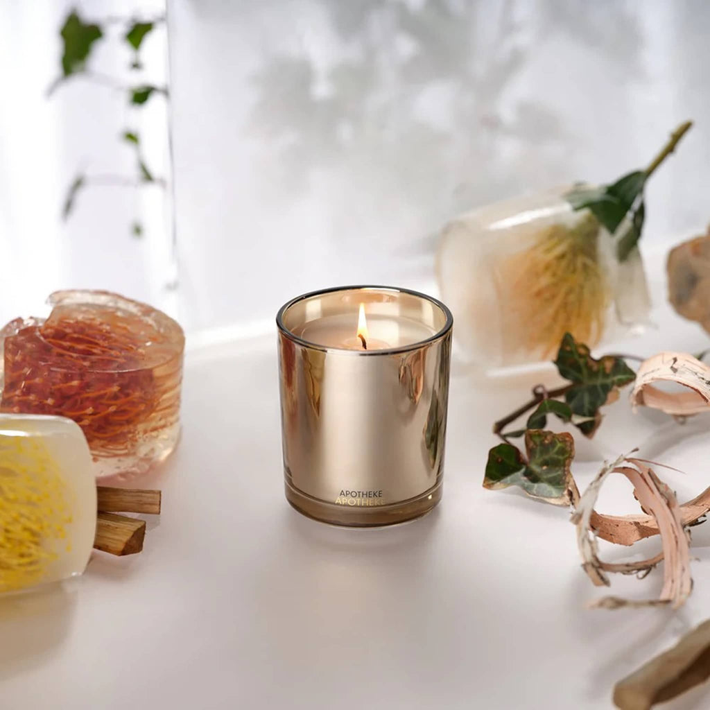 A lit candle in a decorative glass jar on a white surface with flowers and ribbons.