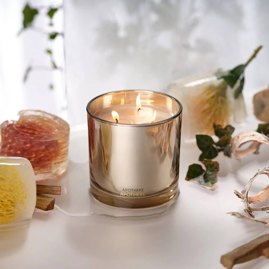 Gold candle in a glass container with decorative elements on a white surface.