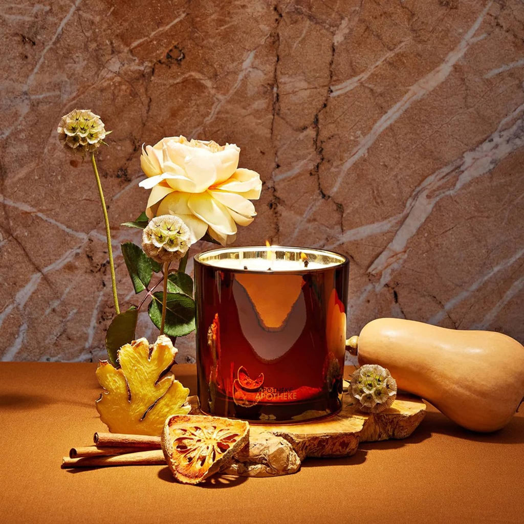 Apotheke Pumpkin Ginger 3-wick candle with fruit and flowers on a stone background.