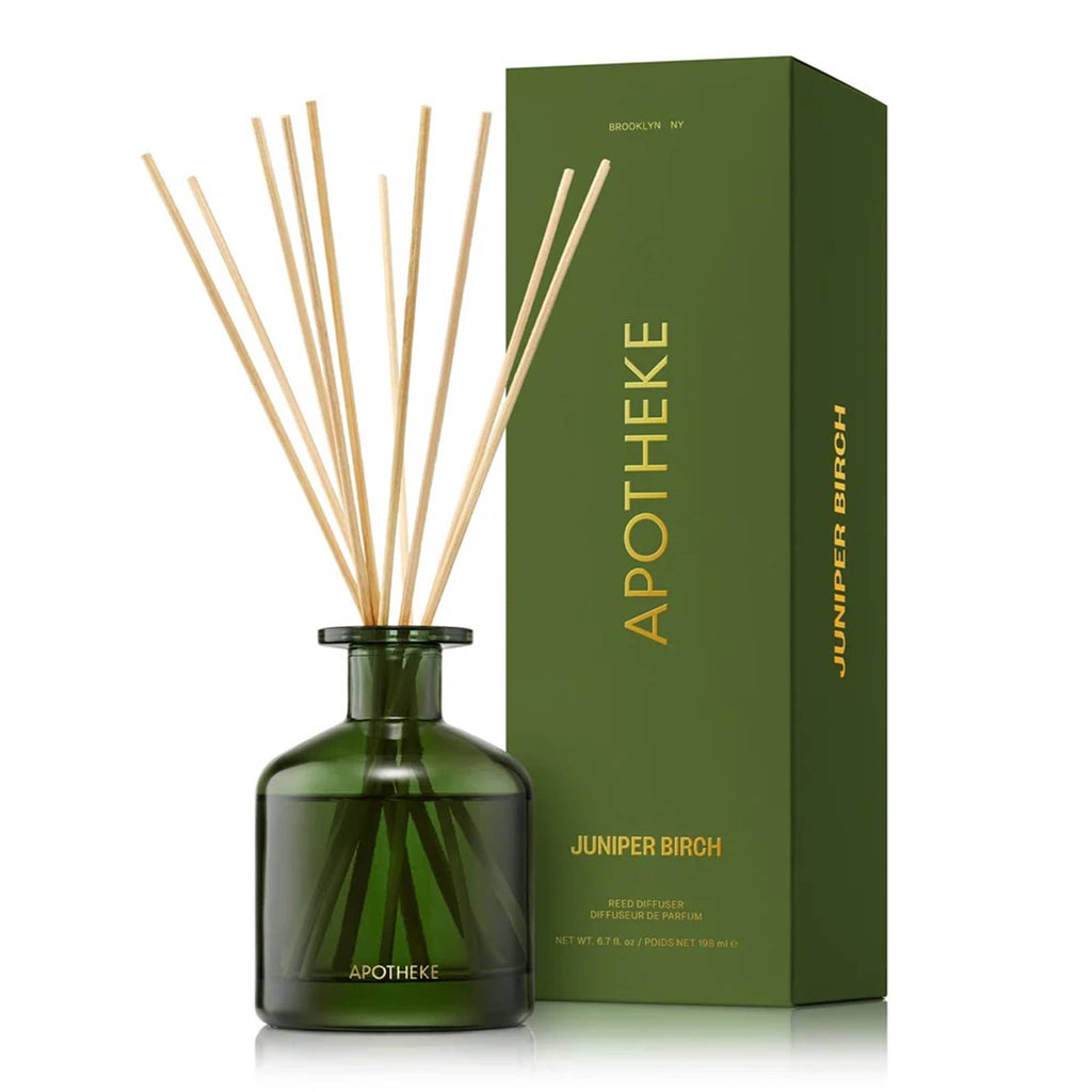 Apotheke Juniper Birch scented limited edition reed diffuser in dark green glass bottle with natural reeds beside matching green box with gold lettering.