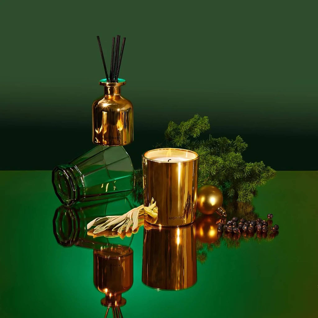 Apotheke Black Cypress scented limited edition mini gold candle and mini gold diffuser duo gift set, on a mirrored green background with botanicals and a green tumbler.