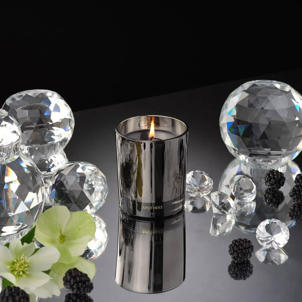 Black candle holder with a lit candle surrounded by clear crystal balls and blackberries on a reflective surface.