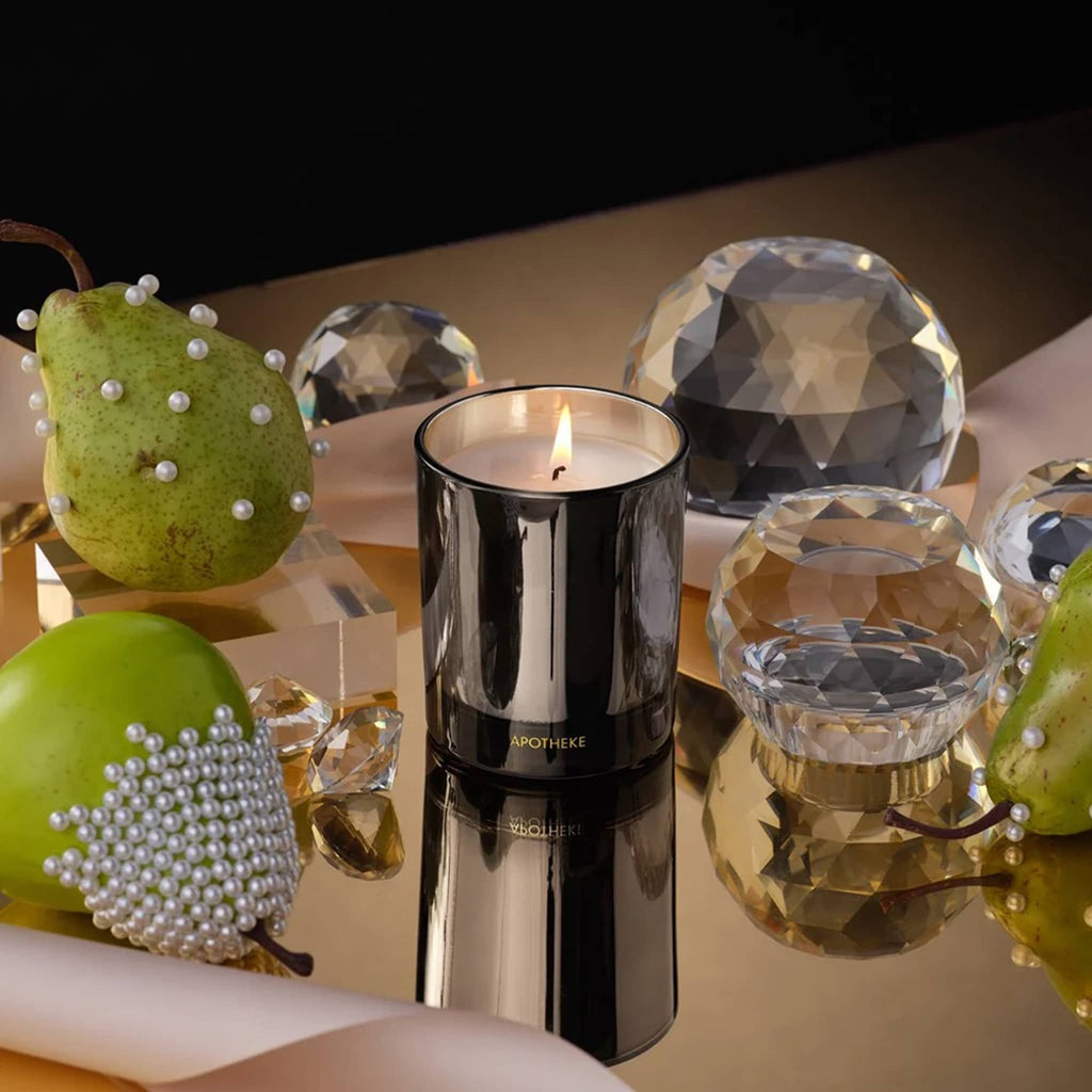 Candle with decorative elements including green pears and crystal balls on a reflective surface.