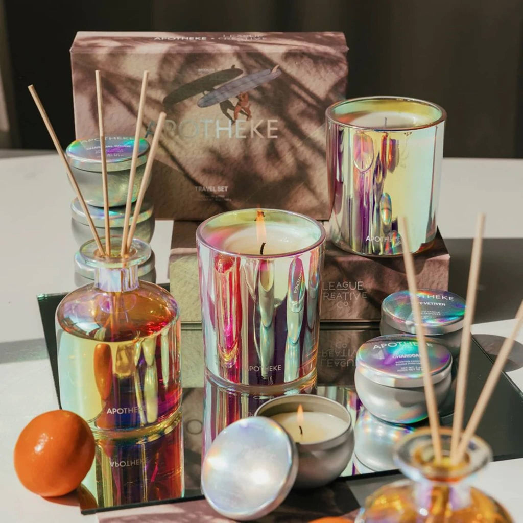 Apotheke x League Creative Co. Bergamot Tangerine scented candles and diffuser in iridescent vessels with illustrated gift boxes on a mirrored tray.