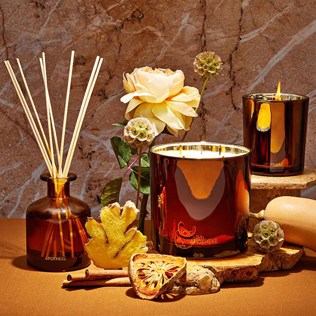 Apotheke Pumpkin Ginger diffuser, 3-wick candle and classic candle with fruit and flowers on stone surfaces.