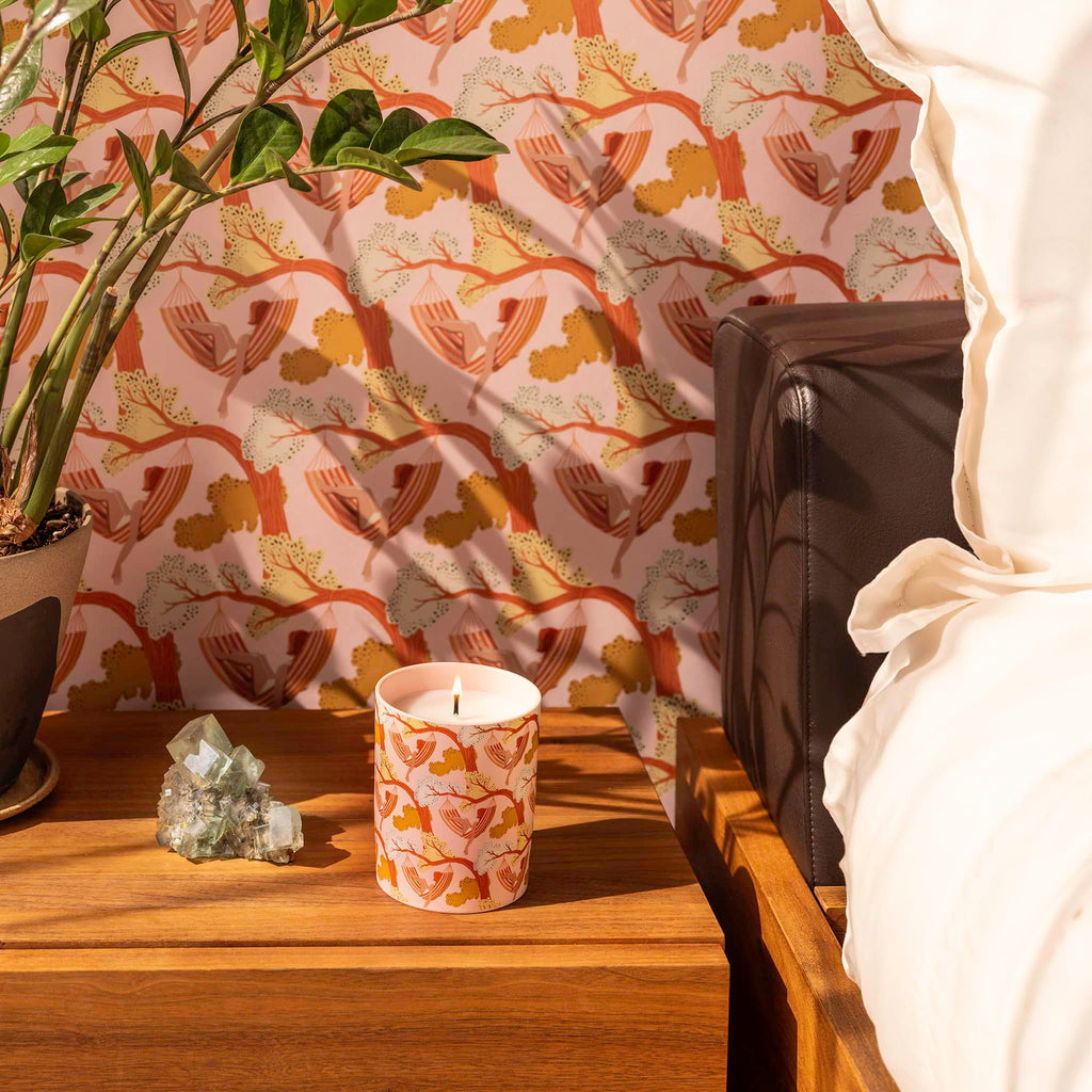 Apotheke x Flavor Paper Sea Salt Grapefruit scented candle in peach ceramic vessel with the Sway print on a bedside table with a crystal and a plant in front of the matching wallpaper.