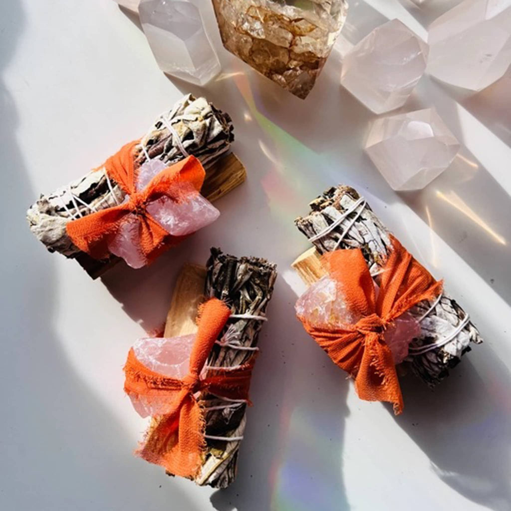 3 bundles of Ark Made Rose Quartz crystal, Palo Santo and Yerba Santa smudge bundles tied with orange chiffon ribbon.