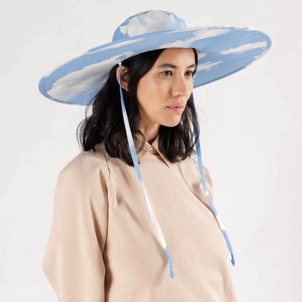 Baggu Clouds print cotton packable sun hat open, on model with tan shirt to show fit.