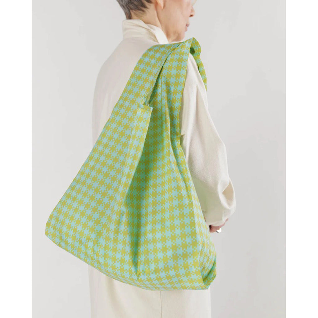 Baggu standard size eco-friendly-recycled ripstop nylon reusable tote bag with mint and pistachio green pixel gingham pattern, on model's shoulder.