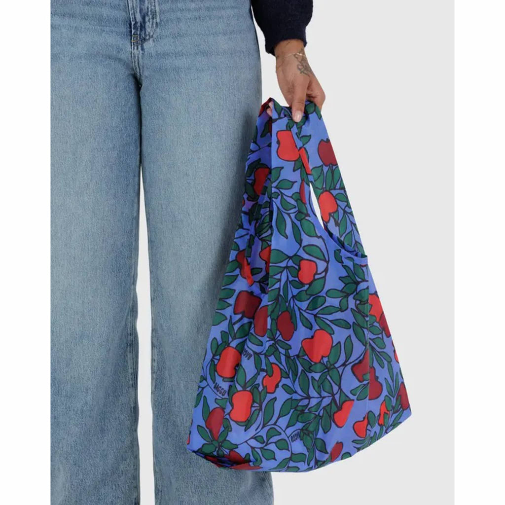 Person holding a blue reusable bag with red apple pattern against a white background.