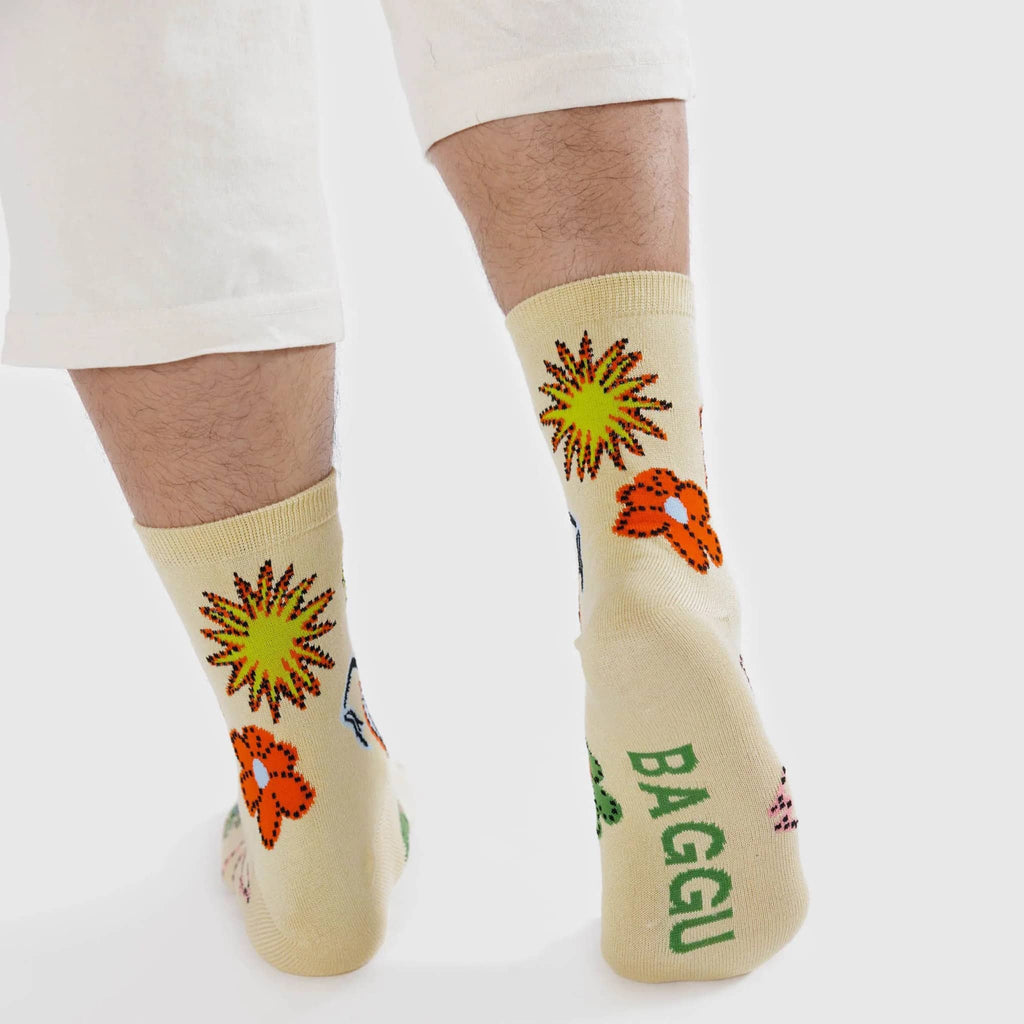 Baggu bamboo rayon unisex crew socks with colorful birds and florals on an ecru background, being worn by a model.
