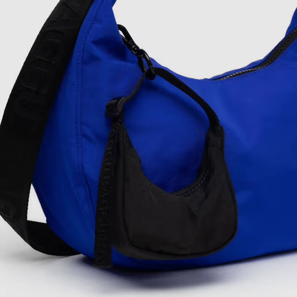 Baggu black crescent bag charm on a larger blue crescent bag, on a white background.