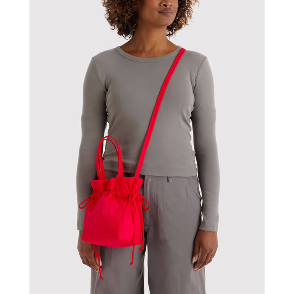 Person wearing a crossbody red drawstring bag  with a gray long-sleeve shirt and gray pants on a white background.