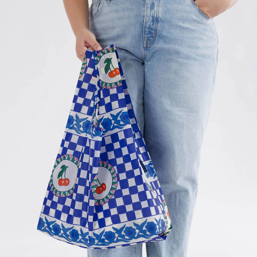 Baggu standard size eco-friendly recycled ripstop nylon reusable tote bag with Cherry Tile pattern, in models hand.